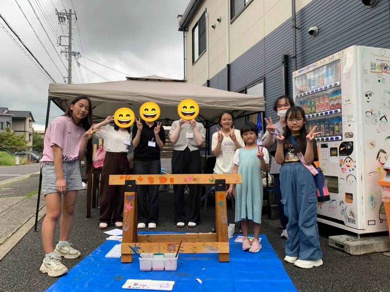 GAUSSプロジェクトで、手形アートで彩った車止めを囲んでピースをする子どもたちと学生ボランティア