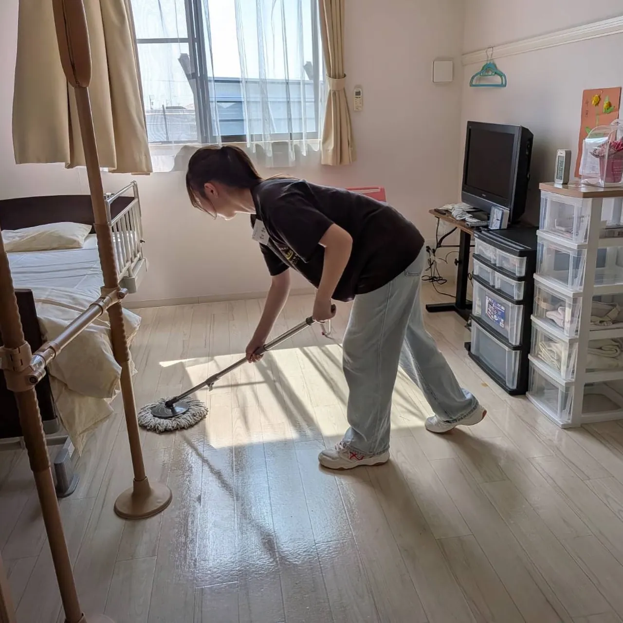 日の差す居室で、床をモップがけする学生さん