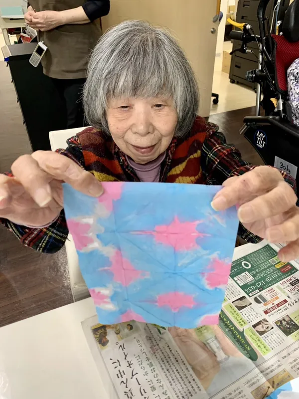 季節の飾りにする染め物の作品を広げて見せるご入居者